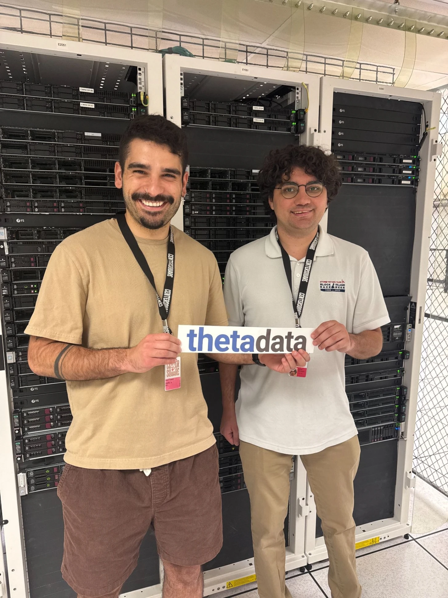 Didier and Bailey holding a Theta Data sign in front of the server racks at the EWR2 colocation site